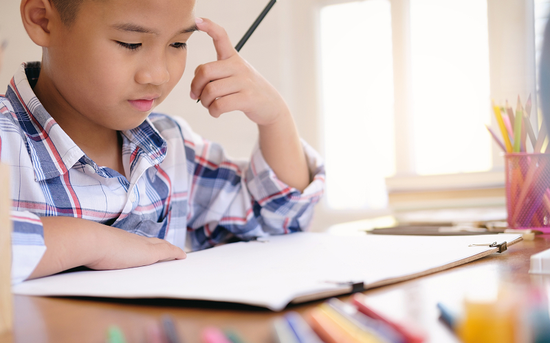 Young boy thinking while doing Chinese second language schoolwork.
