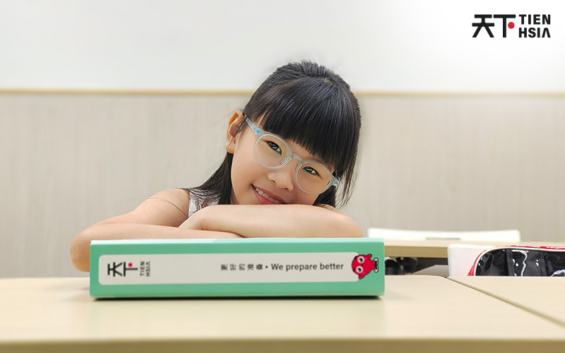 A smiling student in class leaning on a book from Tien Hsia