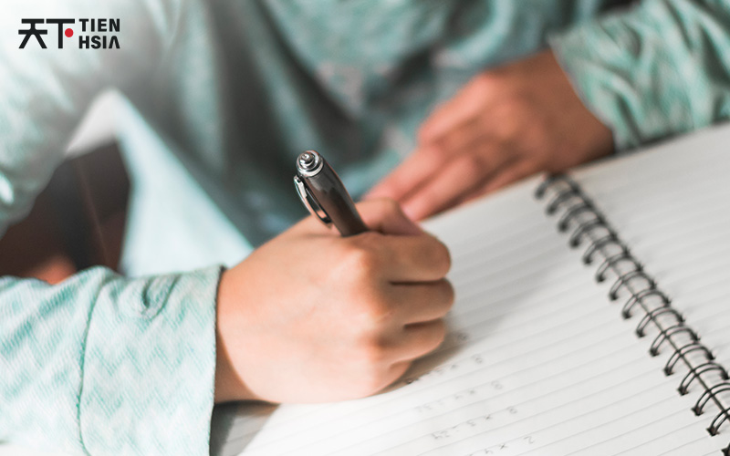 A student writing notes on a pad for O-Level exams.